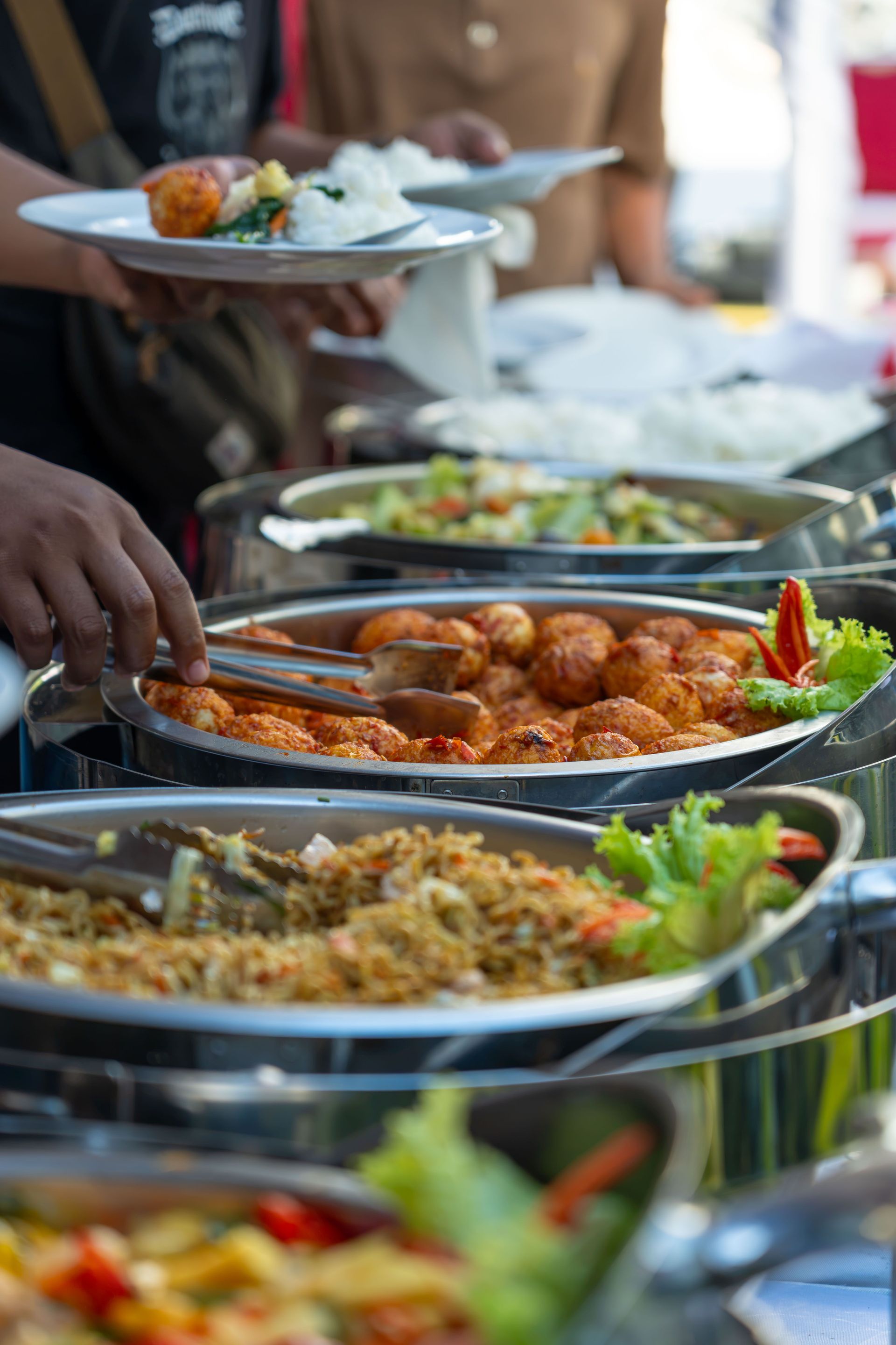 A colorful outdoor buffet scene showcasing a variety of delicious dishes served in stainless steel containers.